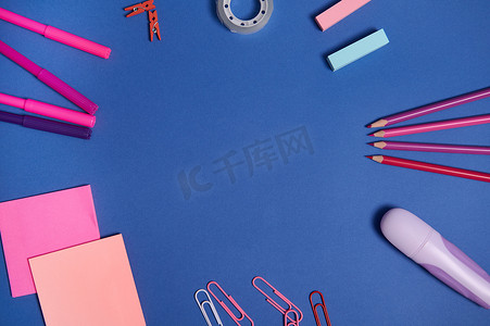 平铺组合物，带有粉色紫色色调的文具或学校用品，散落在蓝色背景上的圆圈中，带有复制空间。