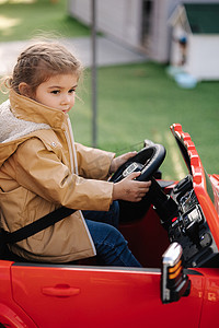 可爱的小女孩骑着一辆红色的电动吉普车在迷你城市中行驶。