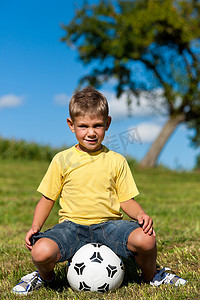 坐在草地上踢足球的男孩