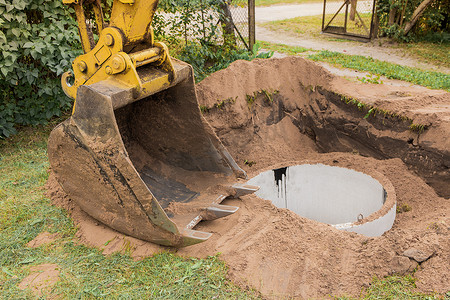 一桶带有一堆沙土的挖掘机在工业区埋下水道混凝土环