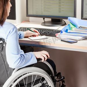 坐在轮椅上工作的残疾或残疾妇女办公桌电脑