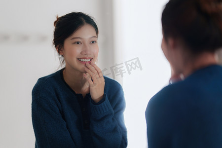 年轻的亚洲女人在浴室里照镜子检查自己的脸的画像。