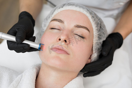 水疗spa摄影照片_治疗师美容师在美容 SPA 诊所对年轻女性的脸进行激光治疗。