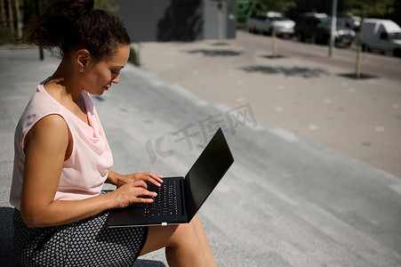 忙碌的自由职业女性、初创企业、上班族的侧面肖像，在喝咖啡休息时间使用笔记本电脑坐在台阶上。