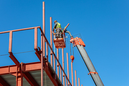 高空作业平台摄影照片_男性建筑工人在升降摇篮中高空作业，打造建筑物的铁架