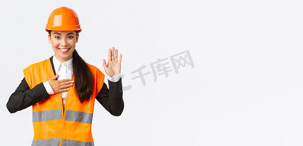 真诚、诚实、自信的亚洲女工程师在建筑区，做出承诺，向客户宣誓，看起来值得信赖，站在安全帽上，说真话，白色背景