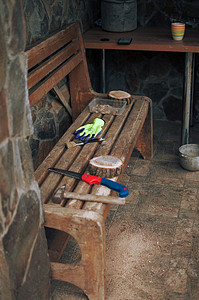 一把旧锤子、一把手锯、防护手套和一条长凳上放着一根带有锯末的圆形松木梁。