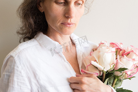 玫瑰花粥摄影照片_中年妇女手捧玫瑰，表情若有所思（裁剪）