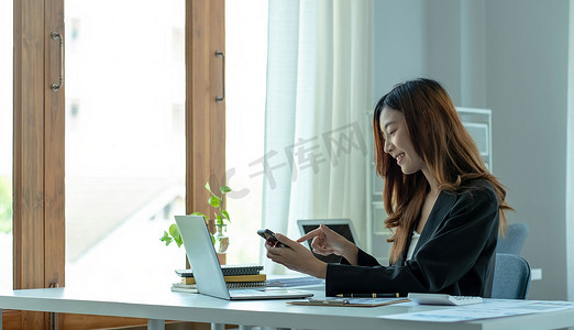 亚洲女商人放松并享受在办公室玩手机的乐趣。
