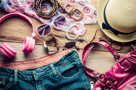 鞋子配饰摄影照片_少女度假时的配饰、帽子、时尚的夏季太阳镜、皮包、鞋子和木地板上的服装。