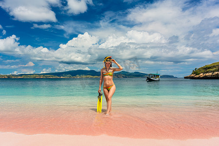 在粉红海滩拿着浮潜设备的漂亮年轻女人