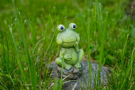 草地设计摄影照片_装饰微型青蛙。花园草地上的小有趣的青蛙雕像。
