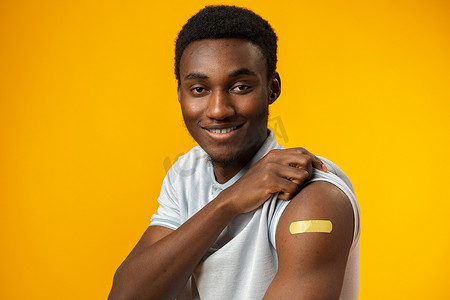 疾病预防背景摄影照片_接种疫苗的非洲裔美国人在黄色背景下展示手臂