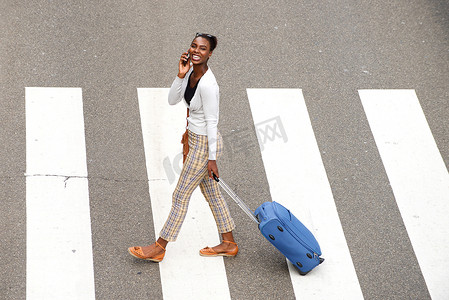 上面是快乐的非洲裔美国女人，带着旅行包和手机走路