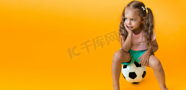 带着经典黑白足球的正宗可爱微笑学龄前小女孩看着黄色背景的相机。