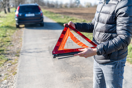 年轻人在一辆破损汽车前的道路上安装了一个橙色三角警示牌。