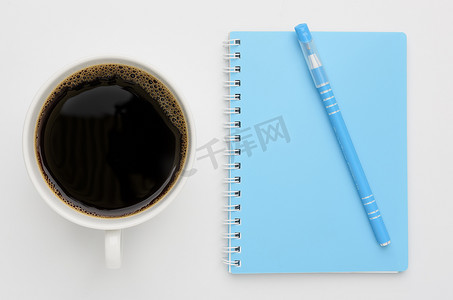 v笔记本摄影照片_加奶咖啡杯和蓝色笔记本，白色背景笔，顶v