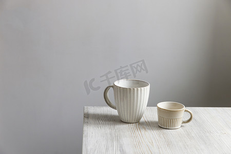 瓷碟摄影照片_米色的桌子上放着两个瓷白色的杯子。