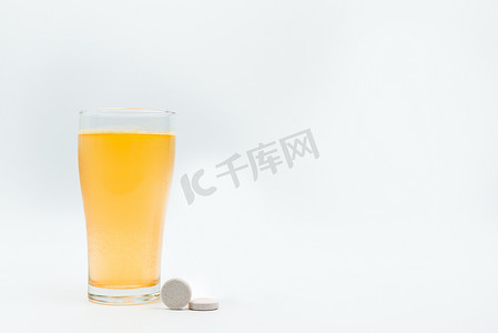 白色背景上的两张泡腾桌和透明玻璃中钙和维生素 C 泡腾片的橙色泡腾气泡。