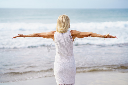 闲暇时光摄影照片_成熟的女人在沙滩上张开双臂，度过闲暇时光，享受闲暇时光