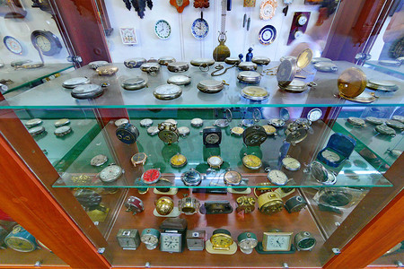 古董玻璃展示柜，有许多不同的时钟机芯，背景还有一个挂钟