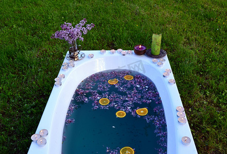 在草地上放着蓝色水和丁香花的浴缸的顶部景色
