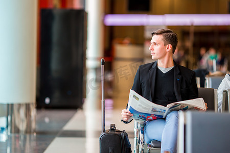 年轻的白人男子在机场等待登机时拿着报纸。