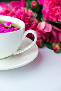 明亮的桌子上有粉色牡丹花和一杯茶的创意布局。