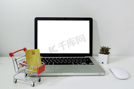 电脑笔记本电脑模拟空白的白色和购物车和信用卡在桌子上。
