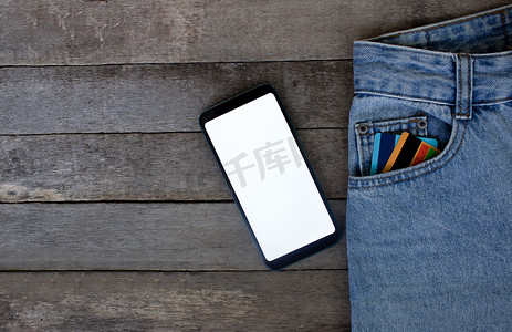 乳酸小口袋摄影照片_模型智能手机与空屏幕和信用卡在木制背景的口袋牛仔裤。