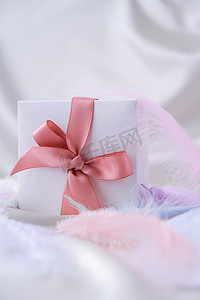白色礼品盒，白色丝绸纹理背景上有粉红色丝带。