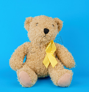 棕色泰迪熊坐着，爪子里握着一条黄色丝带