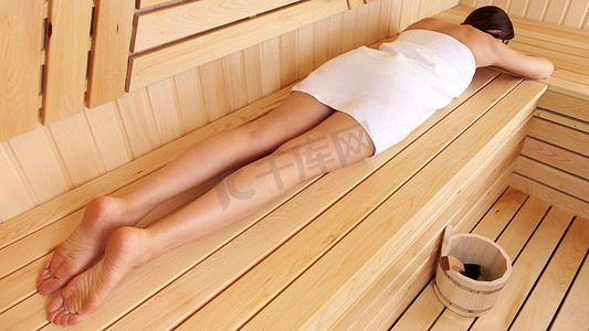 在木制桑拿房里放松的女人躺在长凳上的肚子上，身上裹着毛巾