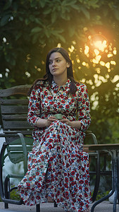 下午，阳光穿过树木，身着花卉图案长裙的拉丁美女坐在花园里，手里拿着一杯咖啡
