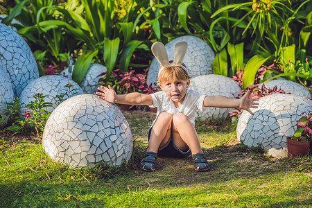 可爱的太阳摄影照片_可爱的小男孩，长着兔耳朵，在户外玩传统的复活节彩蛋。