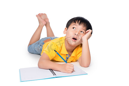 小学生躺在地板上，抬头在笔记本上写字。