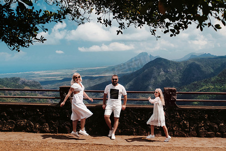 一个幸福的家庭，一个男人，一个女人和一个女儿，在毛里求斯岛的山脉和丛林的背景下快乐地跳跃。毛里求斯岛丛林中的一对夫妇和女儿穿着白色的衣服在非洲行走，