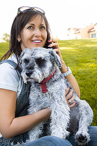 一个快乐的白人女人的肖像，她拥抱她心爱的雪纳瑞狗，通过电话交谈。爱动物的概念。