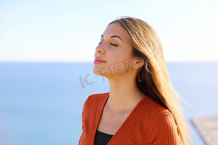 呼吸新鲜空气摄影照片_美丽放松的女孩在蓝色大海的背景下呼吸新鲜空气的特写。