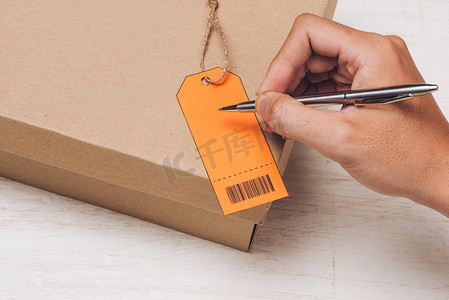 行李标签摄影照片_男性手写在棕色纸包裹的行李标签上