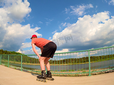 穿着红色 T 恤和黑色裤子在桥上滑冰的直排轮滑手的后视图。