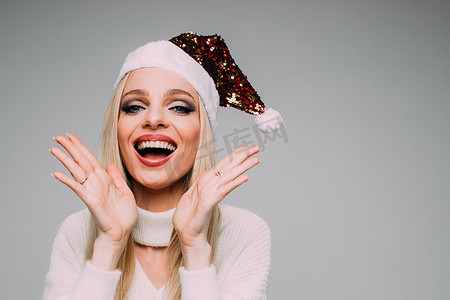 玩美圣诞摄影照片_穿着白色针织毛衣和圣诞帽的微笑漂亮女士玩得开心