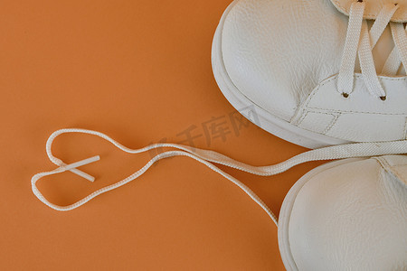 运动白鞋摄影照片_一双白鞋，橙色背景上用鞋带做成心形。