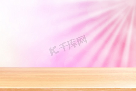粉红渐变摄影照片_空木桌地板上柔和的粉红色散景灯光束闪耀渐变背景，木板空在粉红色散景彩色灯光上，粉红色彩色散景灯渐变软用于横幅广告
