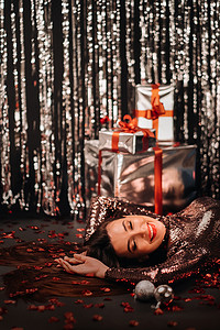 五彩的衣服摄影照片_一个女孩穿着闪亮的衣服躺在地板上的头像，上面是五彩纸屑，上面是心形和礼物