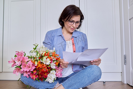 造纸业摄影照片_拿着一束花的微笑中年女性阅读纸