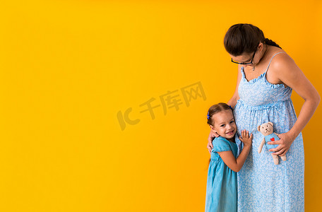 母性、爱情、童年、怀孕、炎热的夏天 — 横幅怀孕的面目全非的母亲期待着婴儿蓝色连衣裙 lillte 女儿女孩兄弟泰迪熊拥抱黄色背景中的妈妈肚子