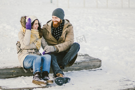 恩爱的年轻人一个留着胡子的男人和一个白人女人在冬天坐在木制楼梯上，在雪地上圣情人节约会圣诞节拥抱和快乐