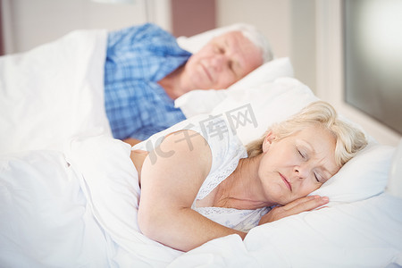 睡觉的枕头摄影照片_与丈夫一起睡在床上的高级妇女