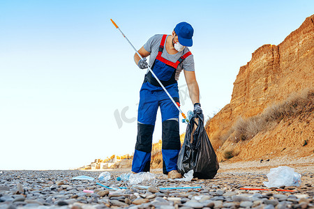男子志愿者用伸展杆在海滩上收集垃圾